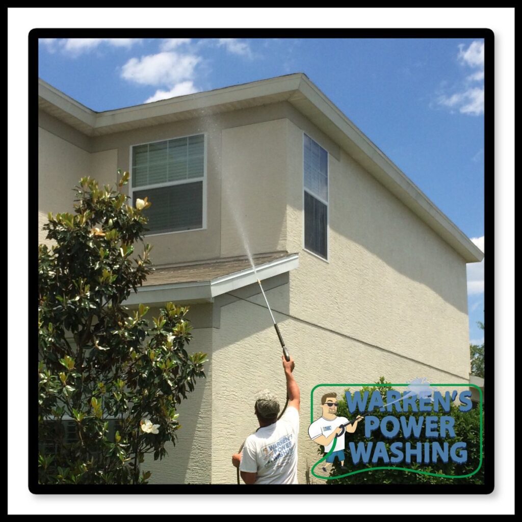 Worker power-washing two-story house exterior